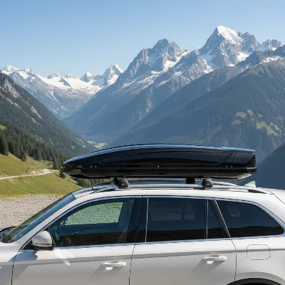 A sleek, aerodynamic black roof box mounted on a silver SUV, parked in a scenic mountain area, demonstrating style and functionality